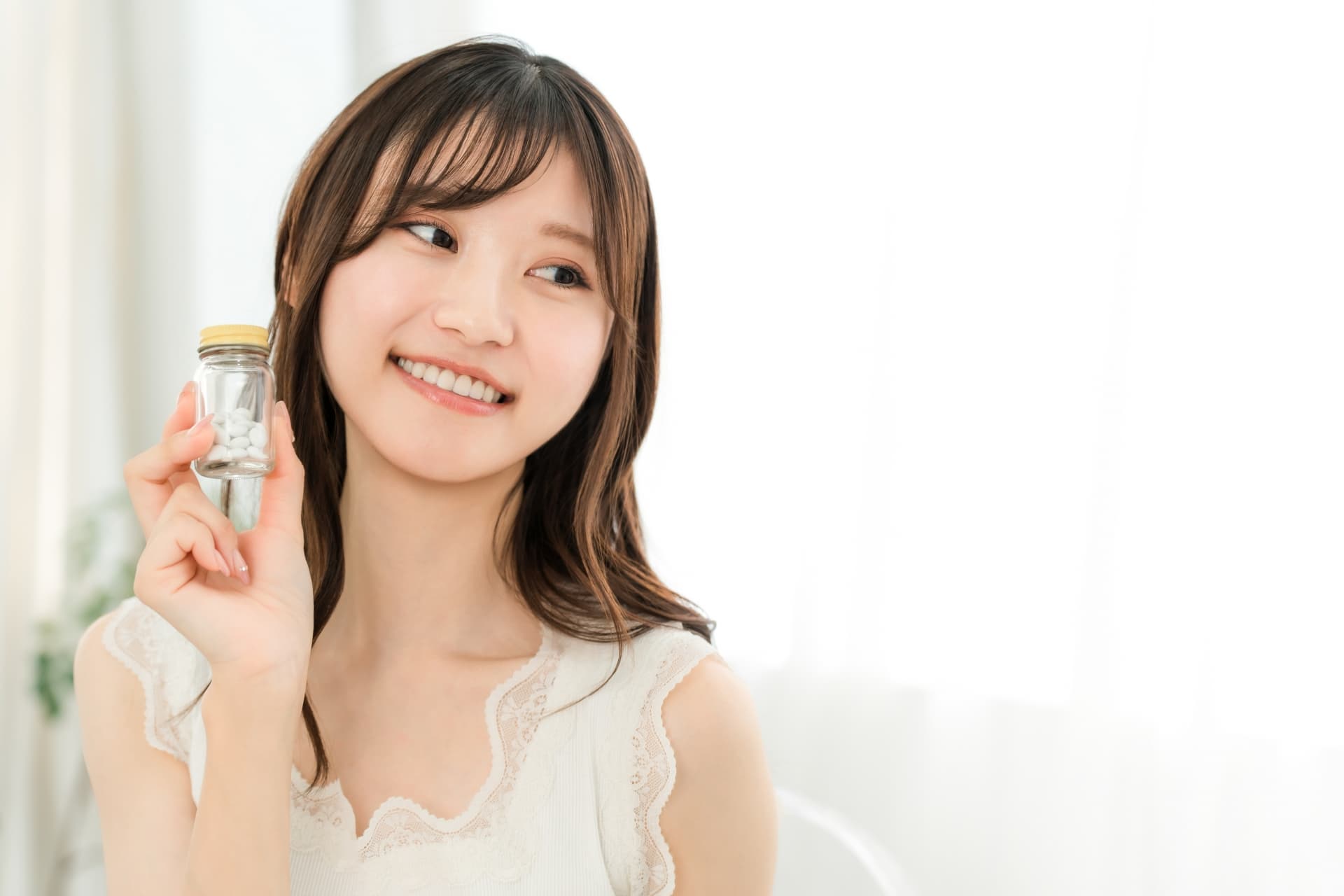薬・サプリメントの瓶を持つ笑顔の女性